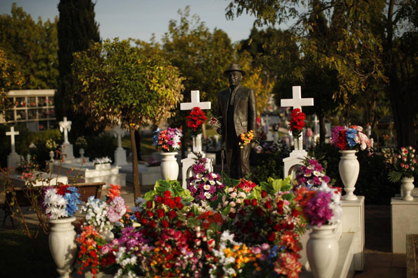 The sculpture of a gypsy man is seen over his tombstone decorated with flowers on All Saints Day in the cemetery of San Gabriel in Malaga, southern Spain, Nov 1, 2011. Catholics mark All Saints Day on Tuesday by visiting cemeteries and graves of deceased relatives and friends. People memorize deceased on All Saints Day