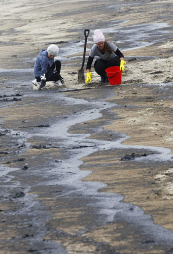 Volunteers remove fuel oil from the stricken container ship Rena that washed up on beaches at Papamoa, near Tauranga October 12, 2011. NZ's oil spills to have long-term impacts
