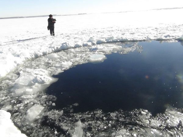 A Russian policeman works near an ice hole, said by the Interior Ministry department for Chelyabinsk region to be the point of impact of a meteorite seen earlier in the Urals region, at lake Chebarkul some 80 kilometers (50 miles) west of Chelyabinsk, Feb 15, 2013. Russia cleans up after meteor blast