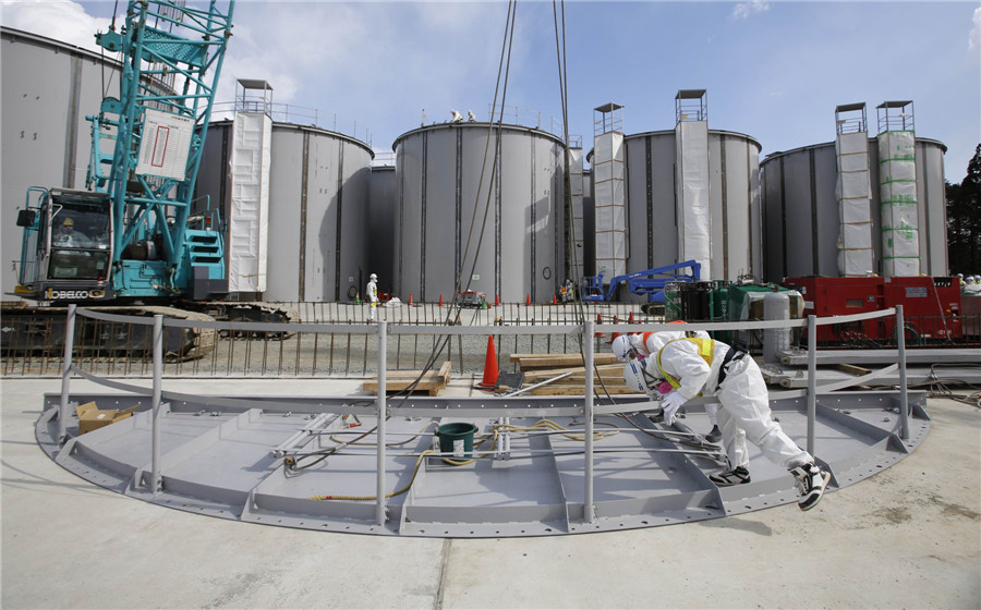 Men wearing protective suits and masks work in front of welding storage tanks for radioactive water, under construction in the J1 area at the Tokyo Electric Power Co's (TEPCO) tsunami-crippled Fukushima Daiichi nuclear power plant in Fukushima prefecture March 10, 2014, a day before the third anniversary of the March 11, 2011 earthquake and tsunami. Visit to Fukushima nuclear plant on meltdown anniversary